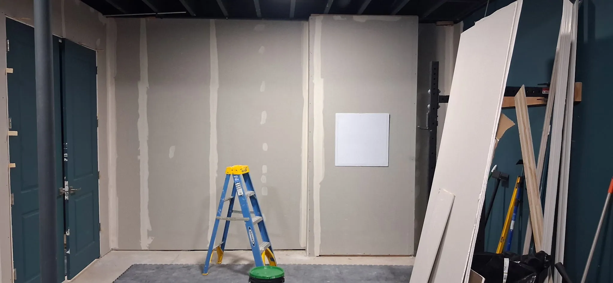 A basement room with drywall hung, taped and floated, and a pair of teal double doors