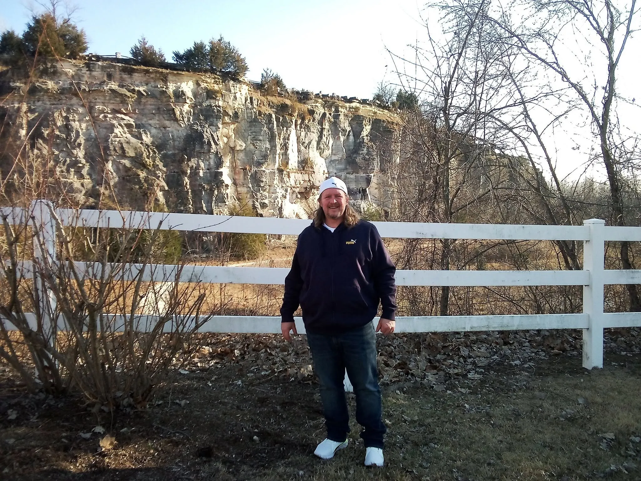Matt Overmann outdoors, wearing a dark hoodie, standing by a white fence